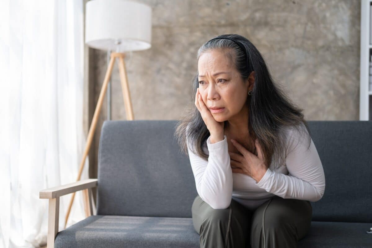 Oudere vrouw ernstige pijn in het hoofd zittend op de bank, gezondheidsproblemen op oudere leeftijd