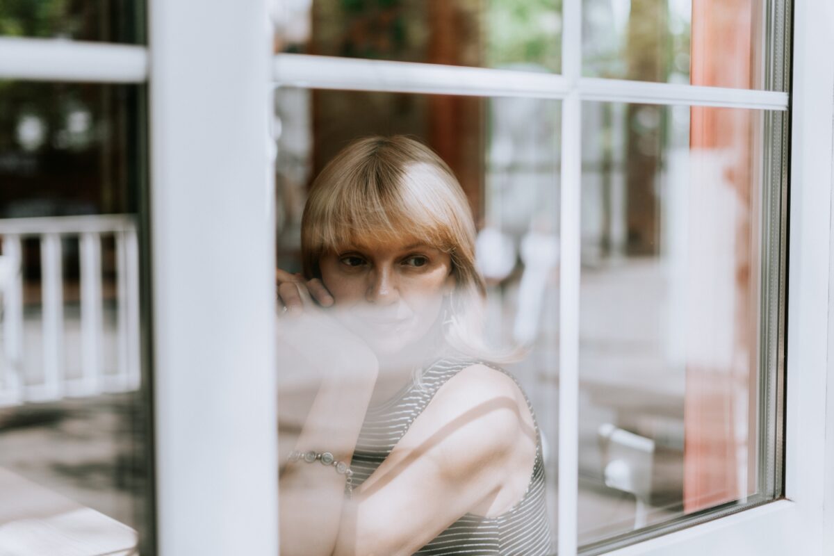 Vrouw zit voor het raam. Droevig en bedachtzaam kijkend. Geestelijke gezondheid en depressie