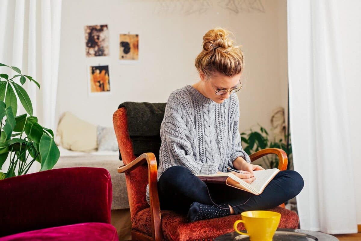 Vrouw die op een dagboek schrijft terwijl ze thuis op een stoel zit