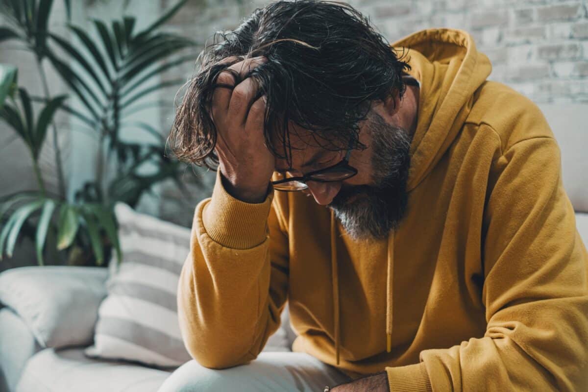 man alleen thuis met hoofd op hand naar beneden kijkend, concept van stress, geestelijke gezondheid