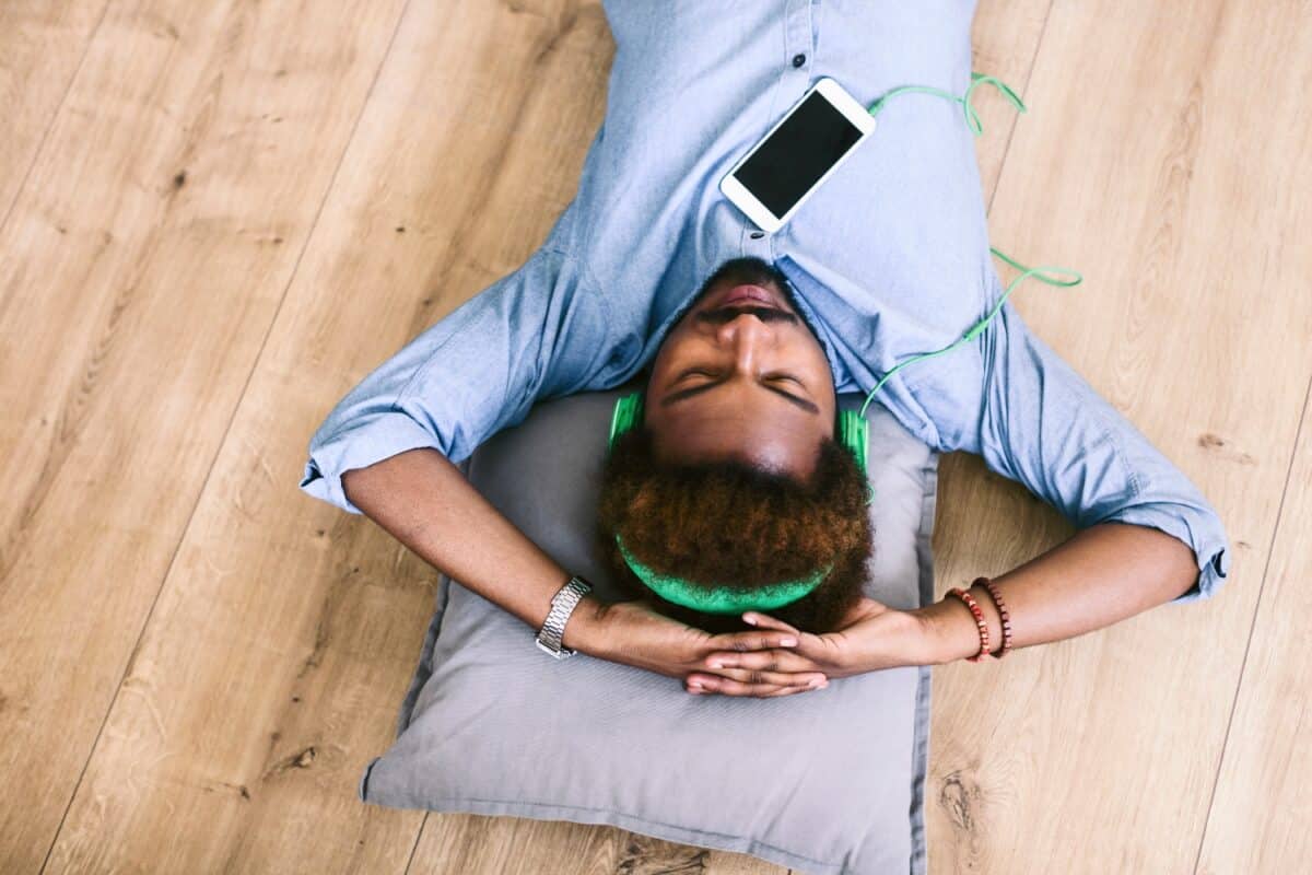 man ligt op de vloer met koptelefoon en smartphone, luisterend naar muziek