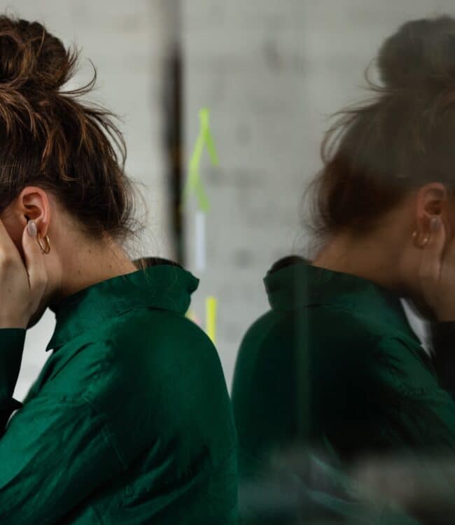 A woman with brown hair in a bun is pictured with her face in her hands and a concerned expression.
