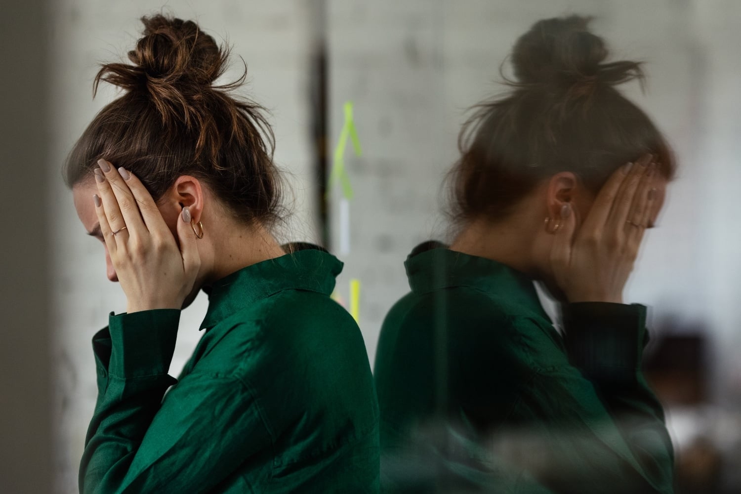 A woman with brown hair in a bun is pictured with her face in her hands and a concerned expression.