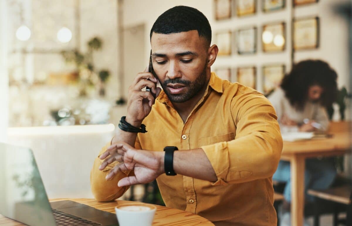 Man sitting and working at a cafe and checking time or phone call with laptop for remote work