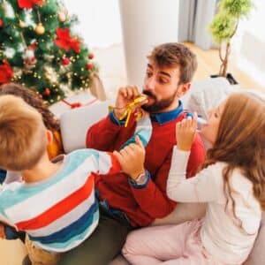 Parents having fun playing with children while spending Christmas at home, blowing party whistles and laughing