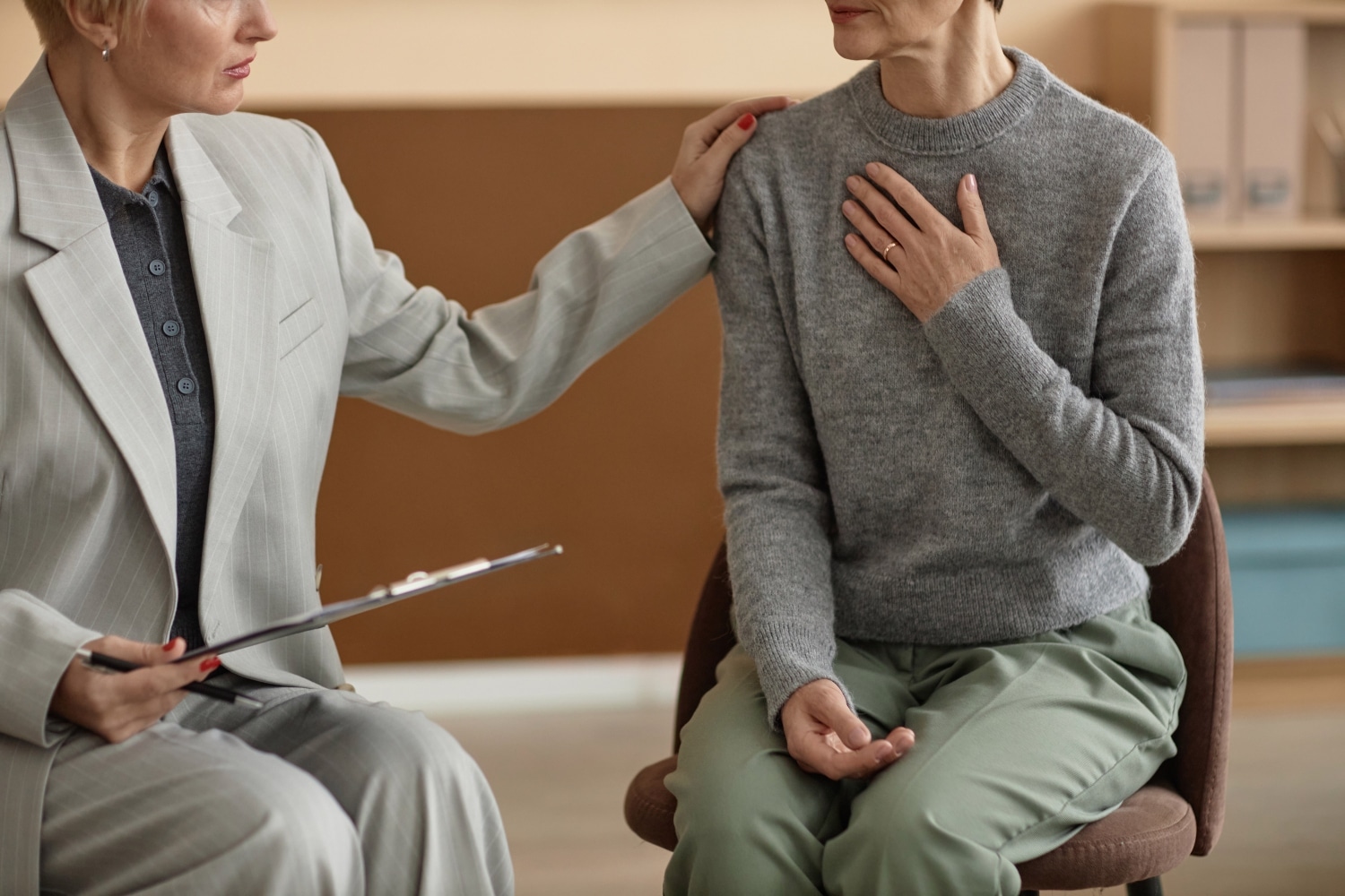 Side view closeup of senior woman sharing mental health struggles with psychologists in therapy session and holding hand to chest