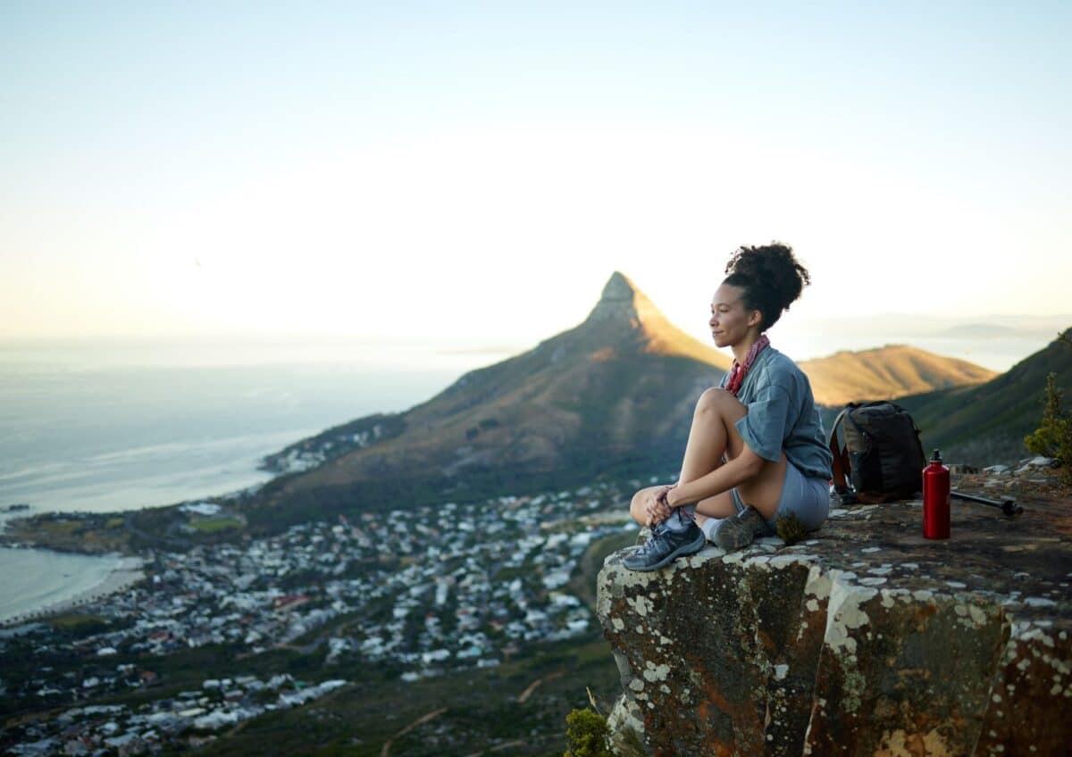 Shot of a woman looking at the view while sitting on a mountain cliff