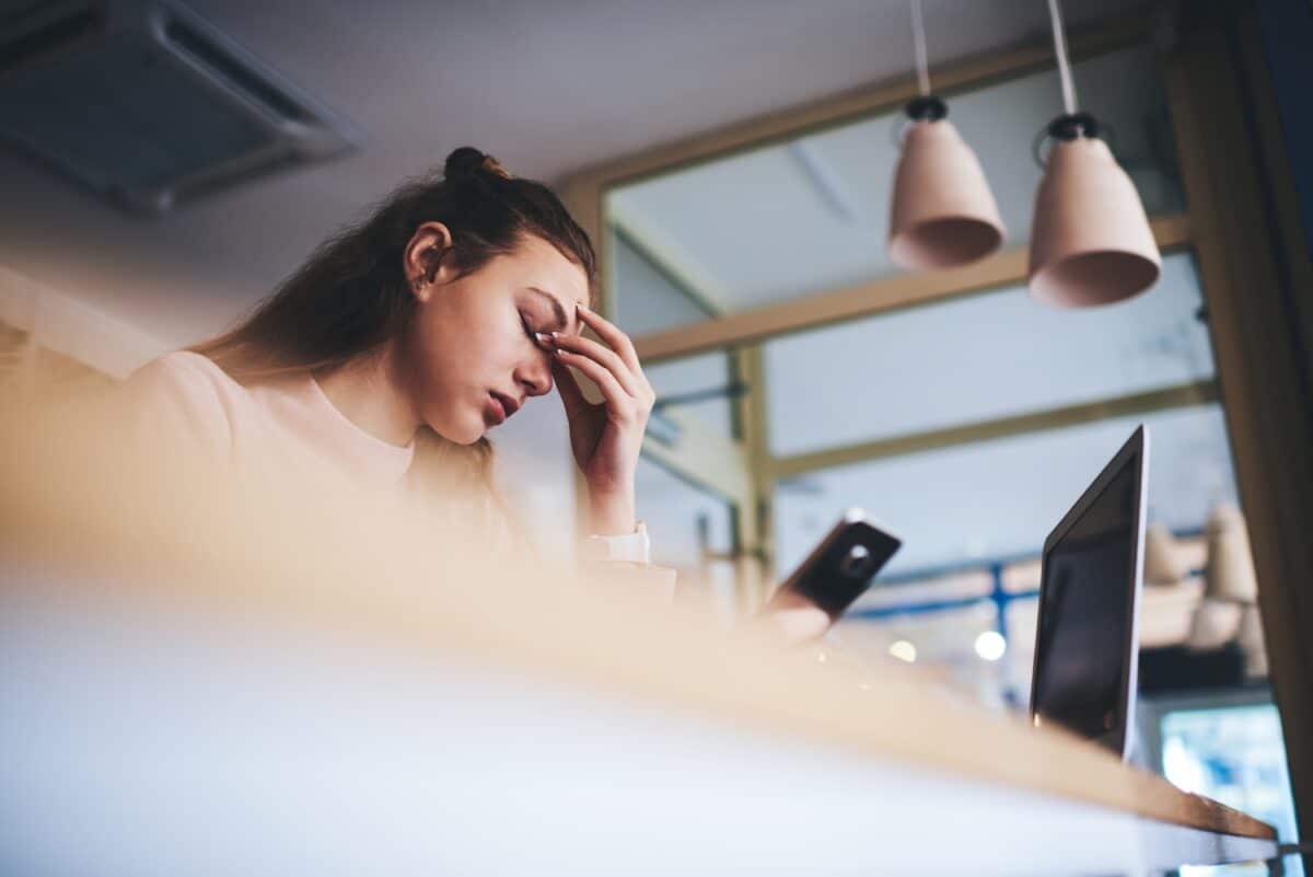 Tired woman using smartphone and laptop for work in cafe