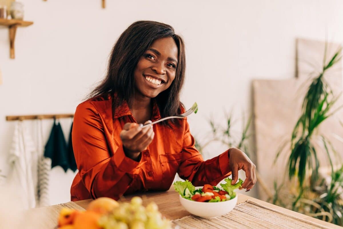 Young happy black woman eating healthy food salad vegetarian on the kitchen at home indoors