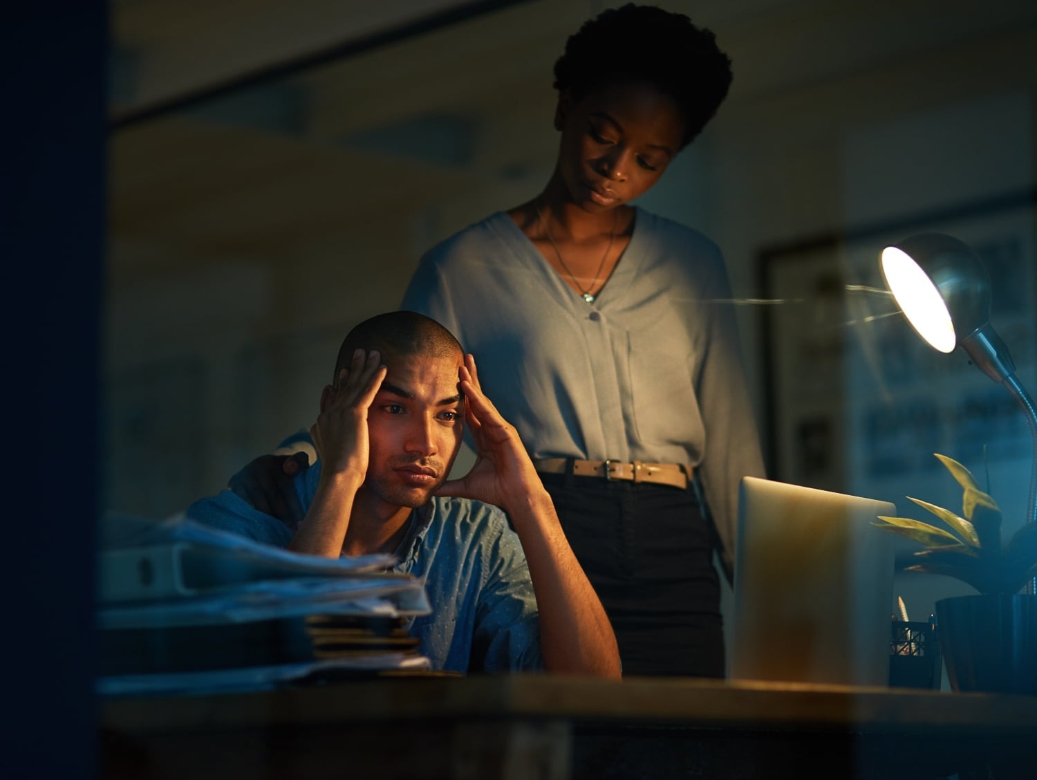 frustrated man working late at night with supportive colleague, concept of burnout