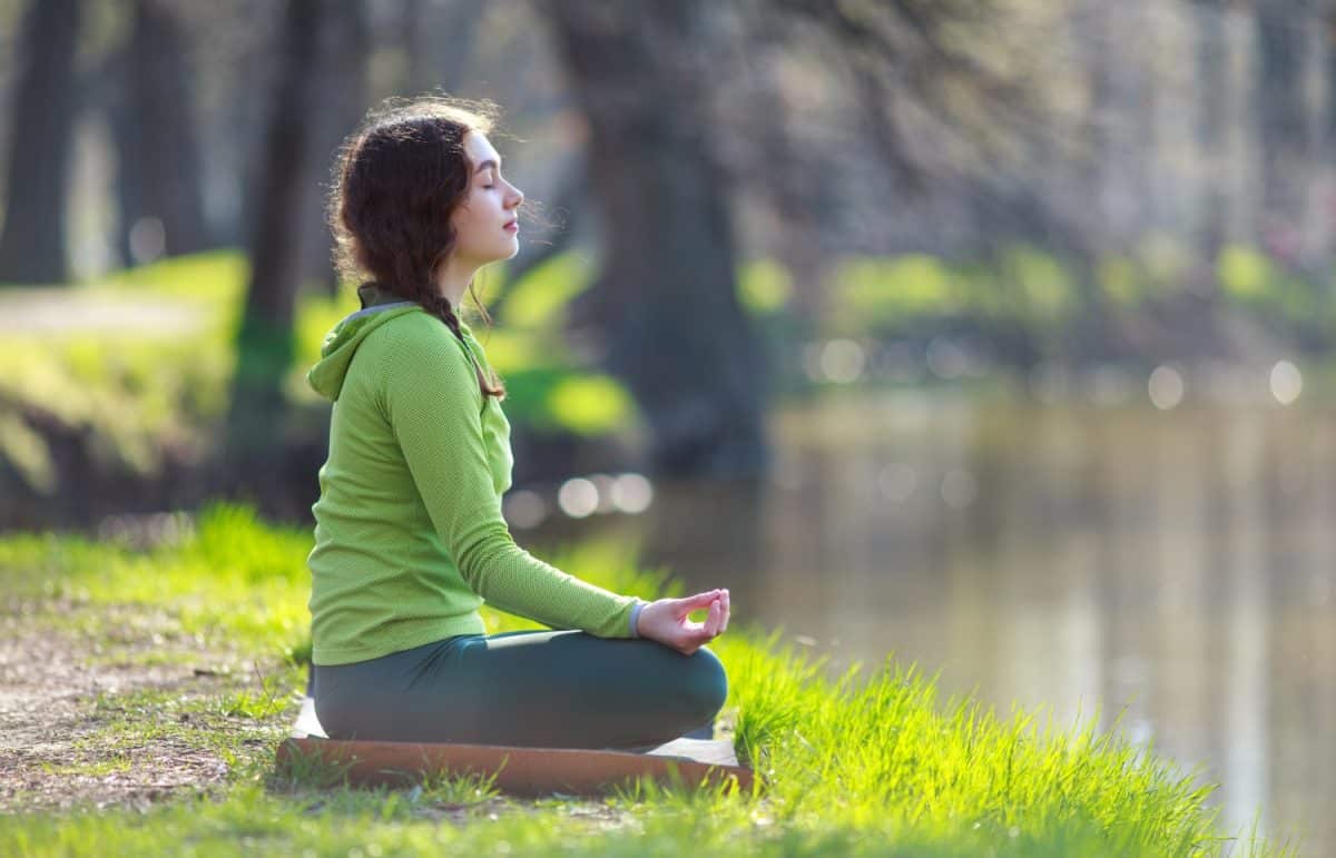 Young woman meditates, practices yoga, on the river bank against the background of beautiful nature