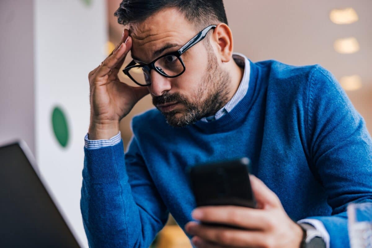 man looking worried, anxious while reading looking at laptop and mobile