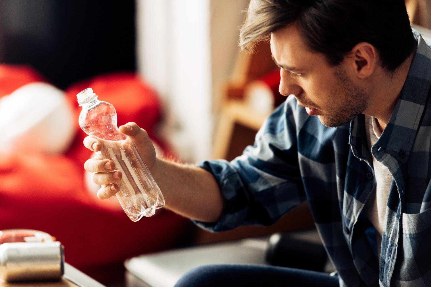man suffering from hangover looking at bottle with water at home