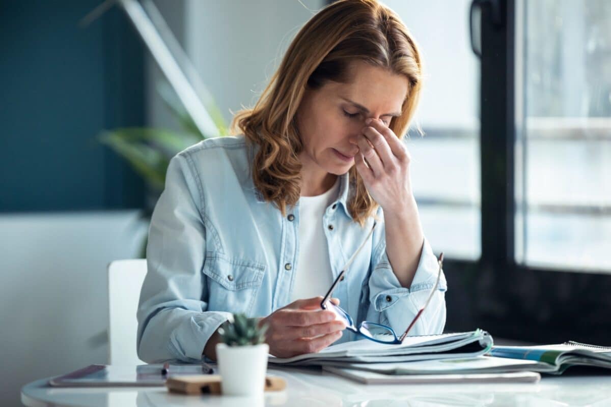 mature woman with headache while working with computer in living room at home, showcasing burnout