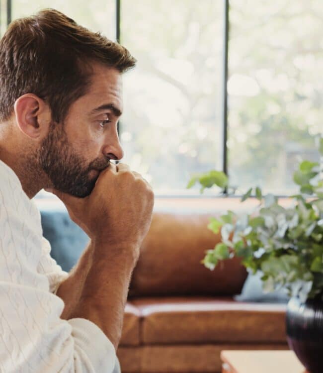 pensive man, sitting alone in the living room looking bored, concept of boredom