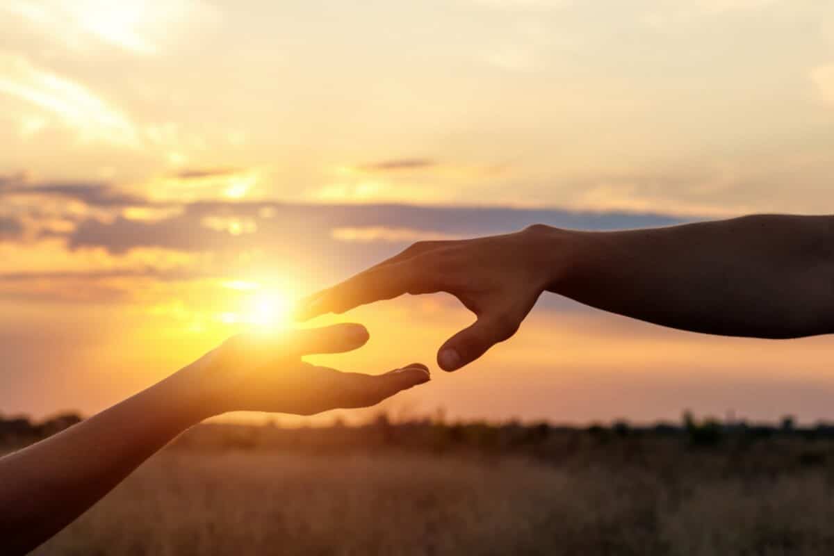 Hands reach for each other in the background of the sunset.