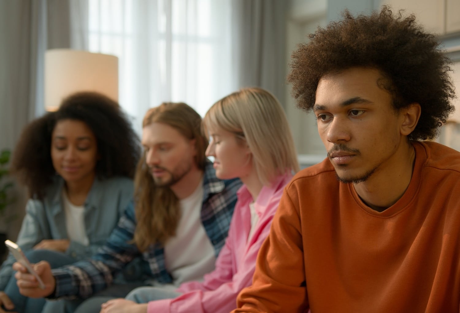 young man looking depressed, anxious while friends are enjoying talking in the background