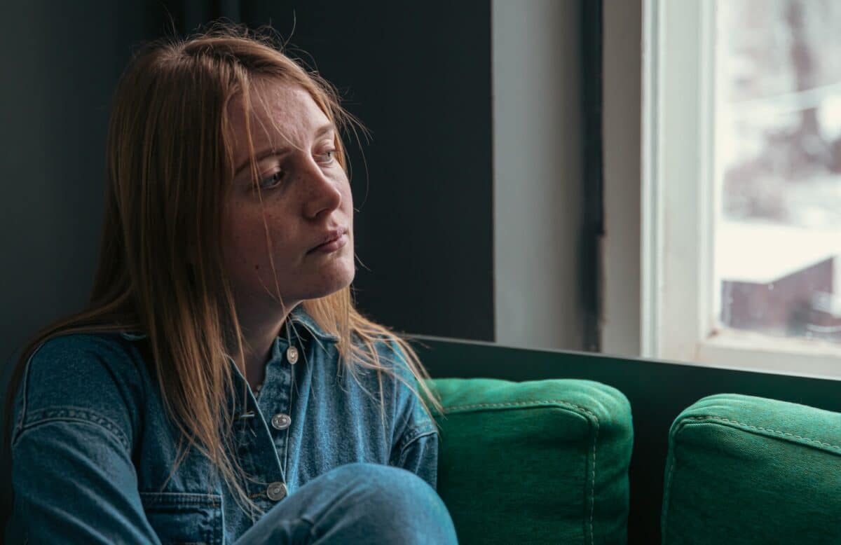 young woman sitting by the window, looking worried, struggling with anxiety, hypervigilance